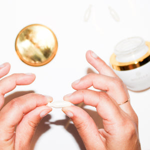 A hand holding a Perfecting Day Serum snipgel pod with the jar in the background.